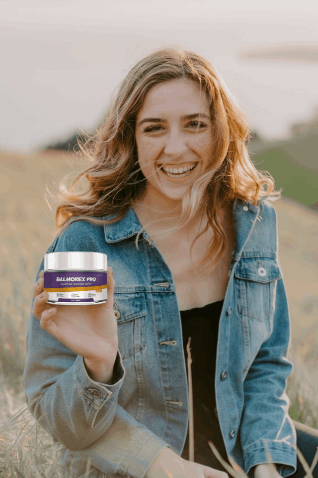 Smiling young woman in a jacket holding a jar of Balmorex Pro Relief and Recovery Cream outdoors to demonstrate effective muscle recovery and fast-acting joint pain relief for active individuals.