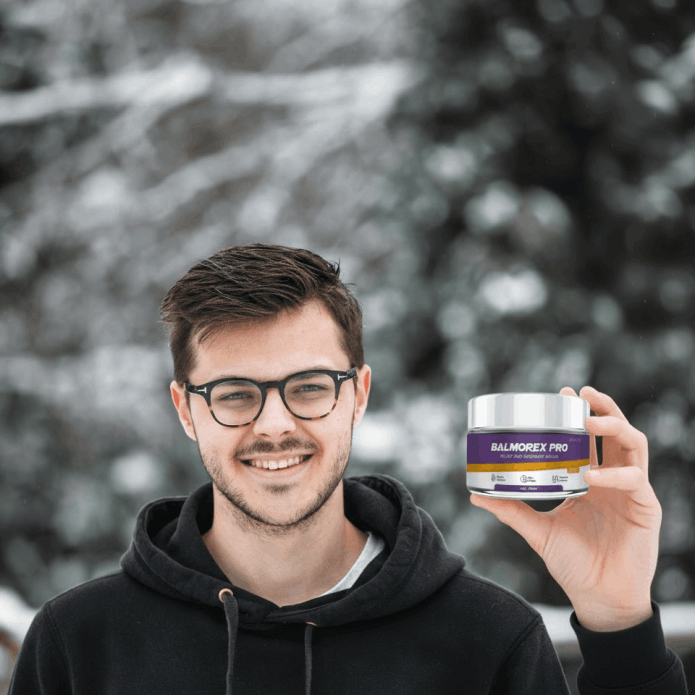 Real-looking customer review photo of a man holding Balmorex Pro cream against a blurred outdoor background, illustrating daily wellness and stiffness relief.
